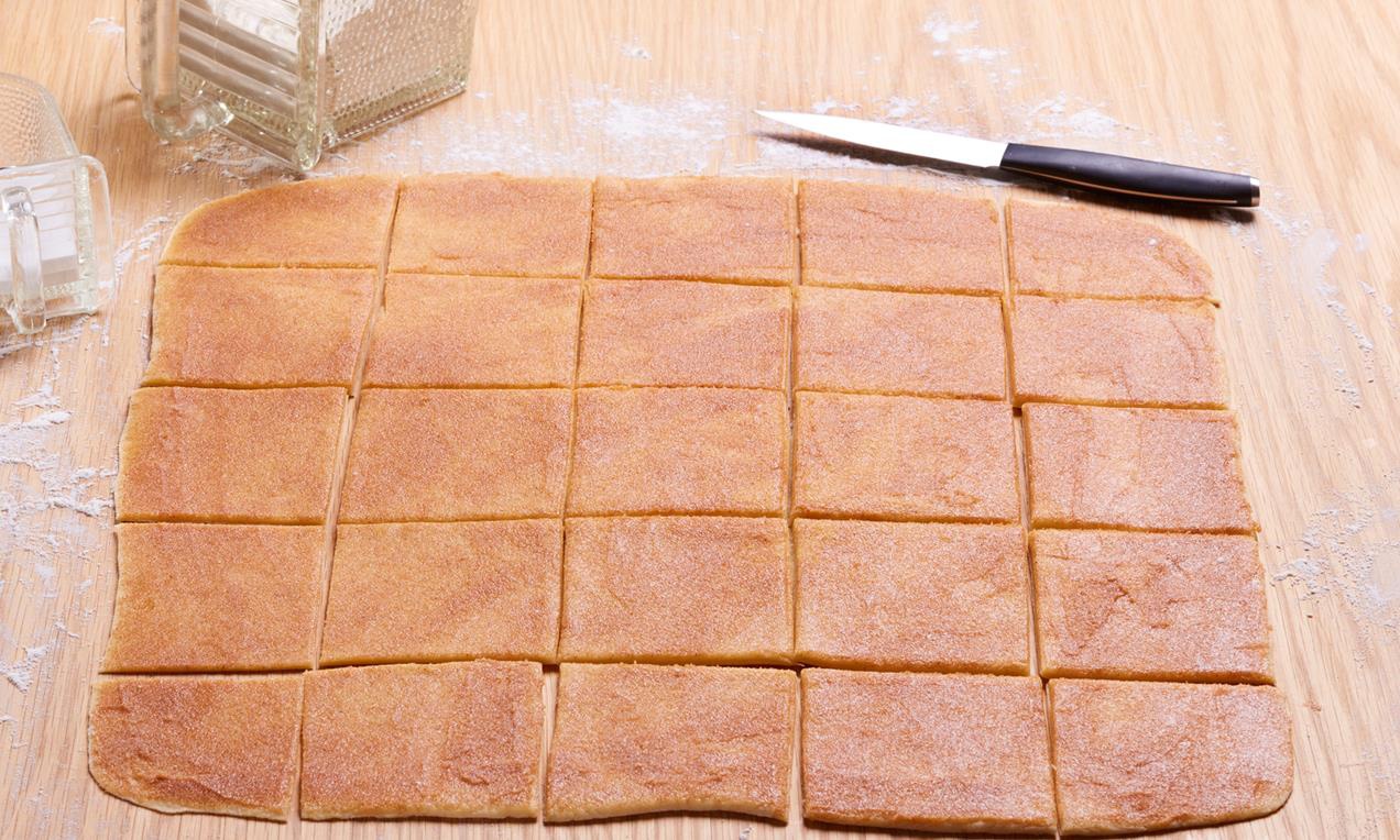 A Édes kenyérlapok süteményt a nyújtódeszkán szeleteljük fel négyzetekre.